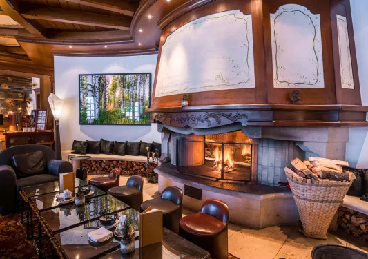 Indoor lounge with cushioned stools around a table with a fireplace behind