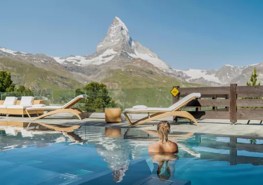 Woman swimming in an outdoor pool looking out towards a tall mountain