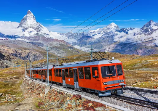 Red train passing through a valley with mountains in the background