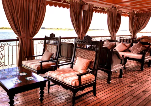Wooden patio with large, red curtains and cushioned chairs looking out towards a lake