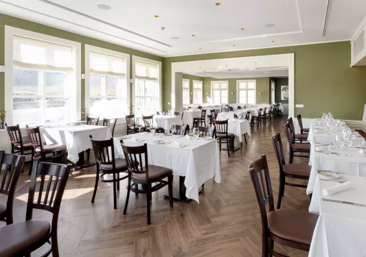 Dining hall in a green room, white white table cloths and large windows