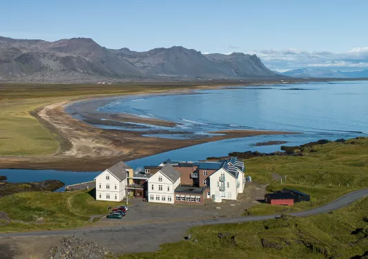 Exterior, sky view of a white and brown hotel building, with a large lake and mountain in the background