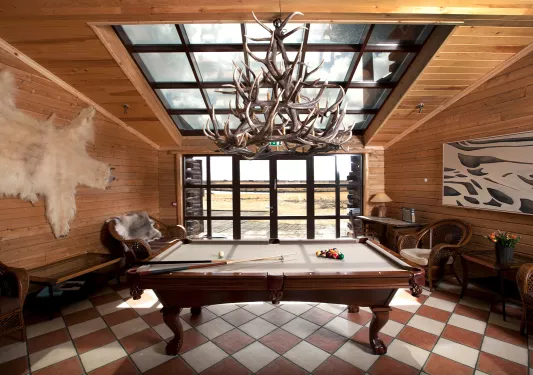 Indoor wooden lodge with a pool table in the center and wooden furniture along the sides
