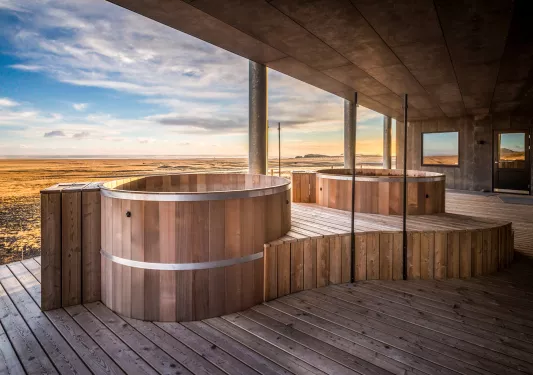 Outdoor wooden sauna with large, stone pillars looking out to an open valley