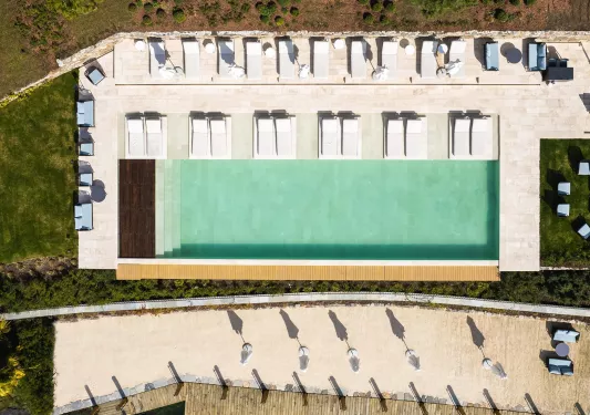 Sky view of outdoor pool surrounded by reclining chairs on a stone walkway