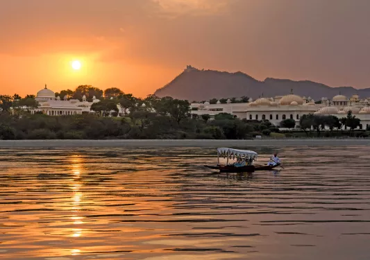 Small boat with a paddle in the middle of an ocean, with large white buildings with the sunset