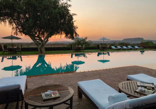Outdoor seating around an outdoor pool, looking out towards the sunset