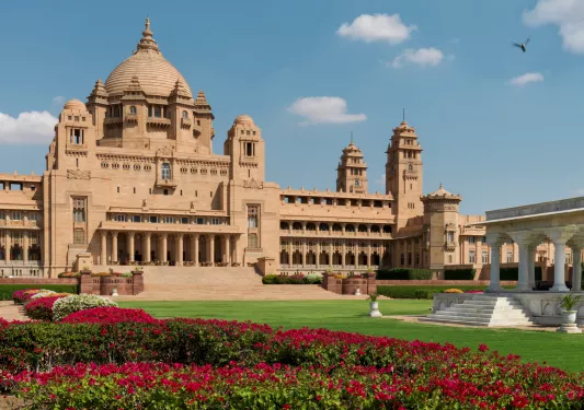 Outdoor view of a palace with a large, open grass area and red flowers