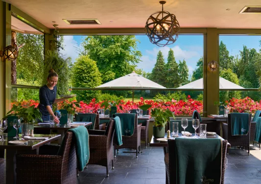 Waitress prepping dining tables with large open windows behind