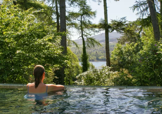 Woman swimming in a pool, looking out to a forest and lake