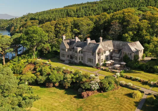 Sky view of stone building with large grass field, surrounded by trees