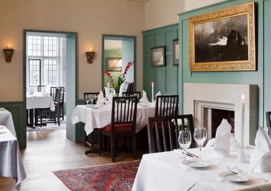Dining area with pictures on the wall, with folded handkerchiefs and wine glasses on each table