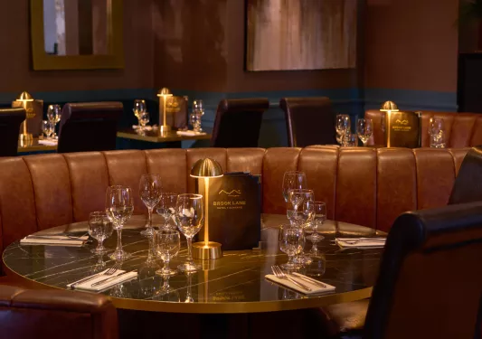 Dimly light indoor dining area with a circular table and wine glasses next to a standing menu