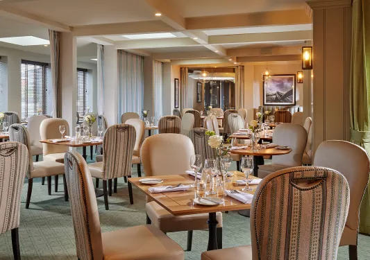Indoor dining hall with tan chairs and wooden tables, with wine glasses on each table