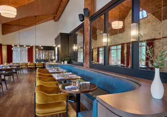 Dining area with a long, gray booth across 4 wooden tables and cushioned chairs on the opposite side