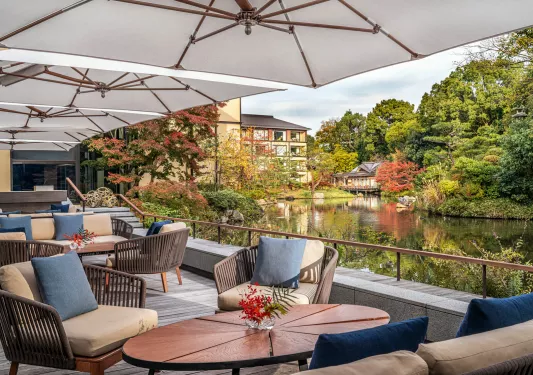 Outdoor balcony with cushioned chairs, looking out to a small lake and forest