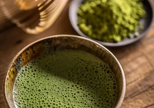 Cup of matcha tea next to a small plate of matcha powder