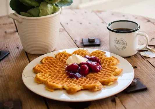 Plate of a waffle with butter and jellied fruit, with a cup of coffee on the right