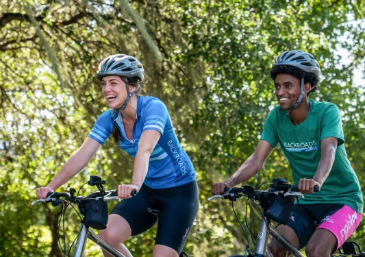 Man and woman riding a bike with large trees in the background