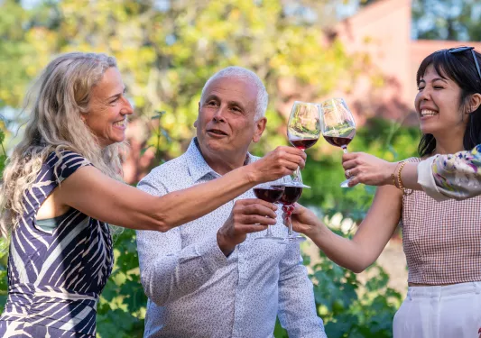 Two women and one man holding up wine glasses and smiling