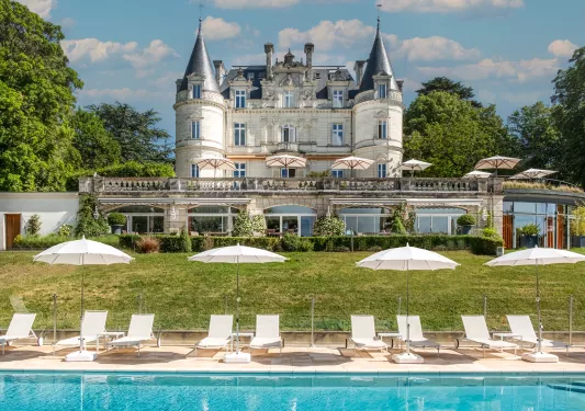 Outdoor pool with white chairs surrounding it, with a castle-like building in the distance