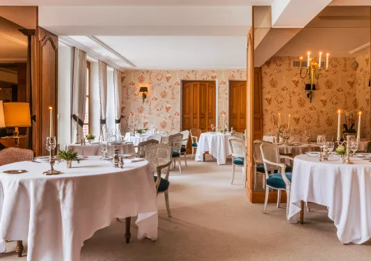 Indoor dining area with flower wallpaper, white dining tables, and two candles on each table