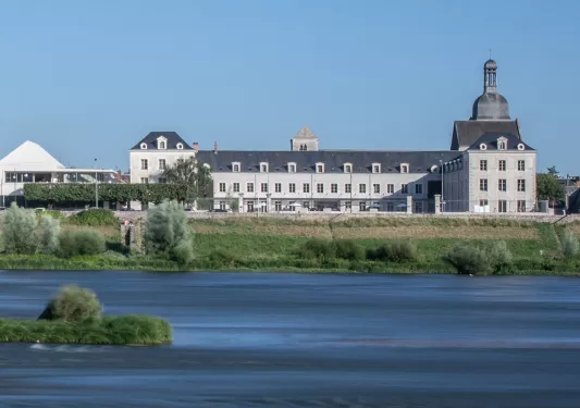 Wide, exterior view of a long hotel building behind a small lake