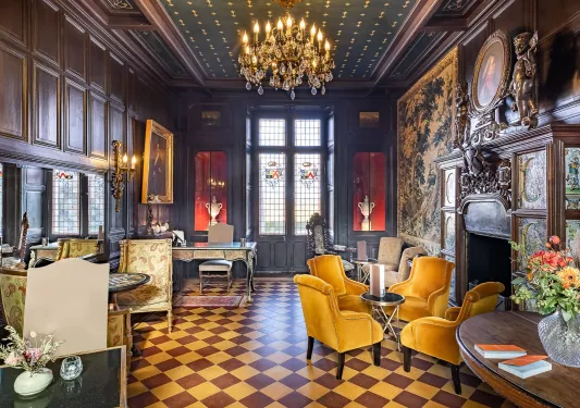 Indoor foyer with brown checkered flooring, cushioned chairs and a candle chandelier hanging from the ceiling