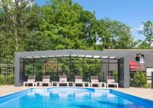 Outdoor pool with brown chairs under a glass canopy covering