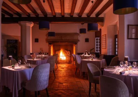 Indoor dining hall with small lamps on each table, and a fireplace in the back