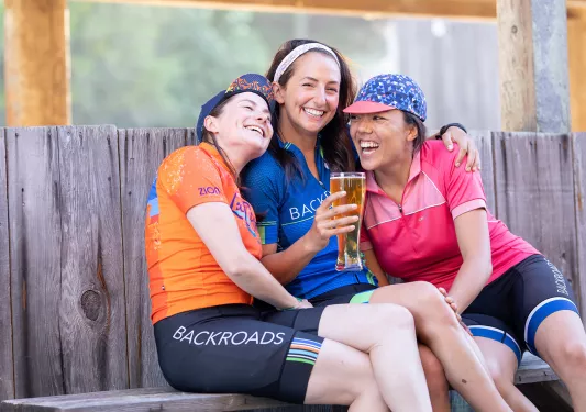 Three women smiling and hugging while holding up a glass of beer