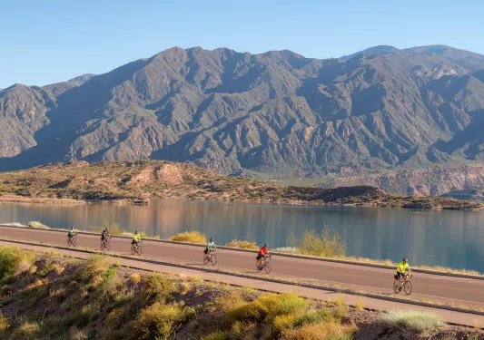 people biking down a road by a mountain range