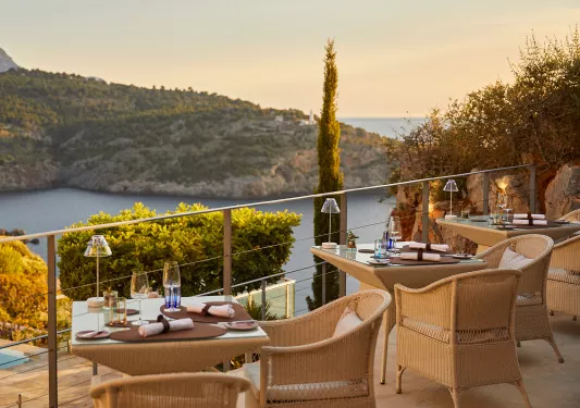 Outdoor patio with woven chairs and glass tables, looking out to a lake