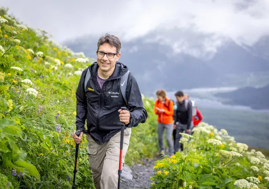 Man with walking sticks climbing up grassy hill