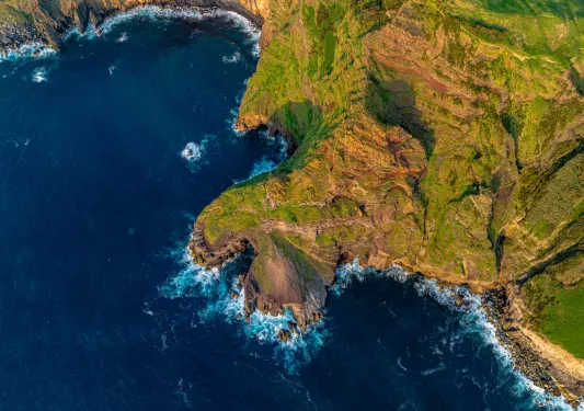 Sky view of a cliff covered in grass, next to the ocean