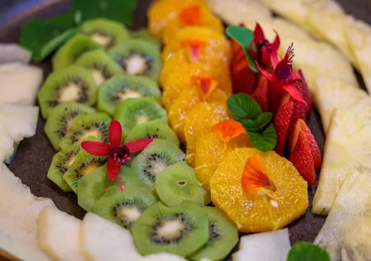 Plate full of sliced fruits, including kiwi, orange, strawberries and pineapple
