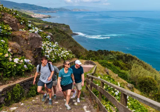 # men and 1 woman walking up a flight of stairs on a dirt path sitting on top of a cliff
