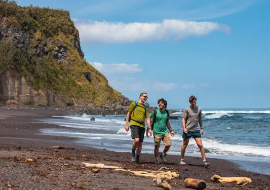 Three men walking on a beach, with a large cliff in the background