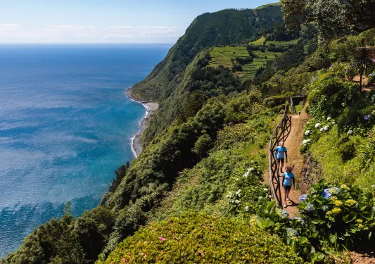 Two people walking on a dirt path along a cliff looking out to the ocean