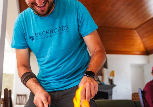 Man in a blue t-shirt smiling as he's cutting into a dish of food