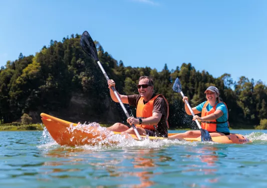 Man and woman smiling in a kayak while paddling in the middle of a lake