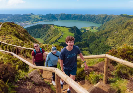 Three people walking on a dirt path that is on top of a hill, with a large valley in the background