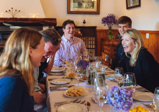 Group of men and woman laughing around a dinner table in a dining area