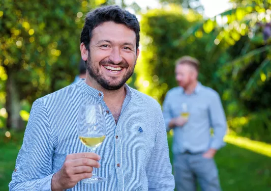 Man smiling at the camera while holding up a glass of wine