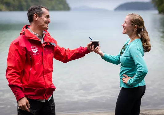 Man and woman smiling while passing each other a mate cup