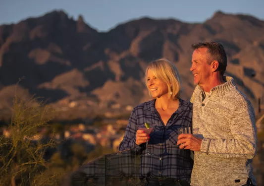 Man and woman smiling while holding martini glasses, looking out to large canyons