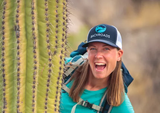 Woman smiling while wearing a backpack, appearing behind a cactus