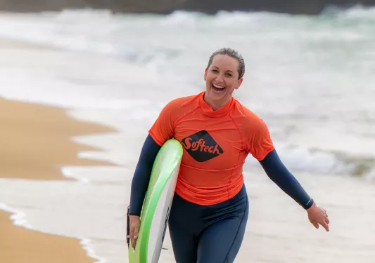 Backroads guest coming out of the ocean with a surf board