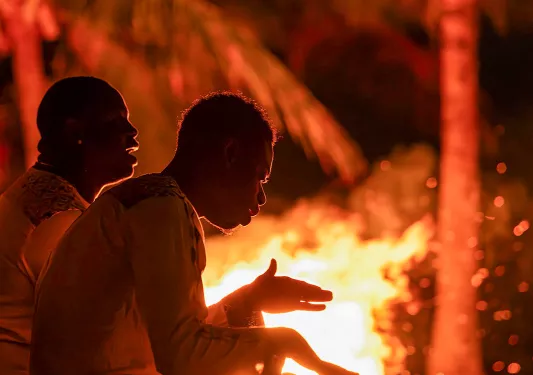 Two men playing bongos around a campfire