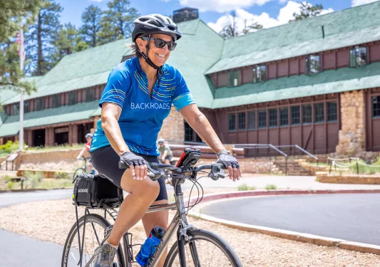 Woman riding a bike with a large, lodge-style building in the background
